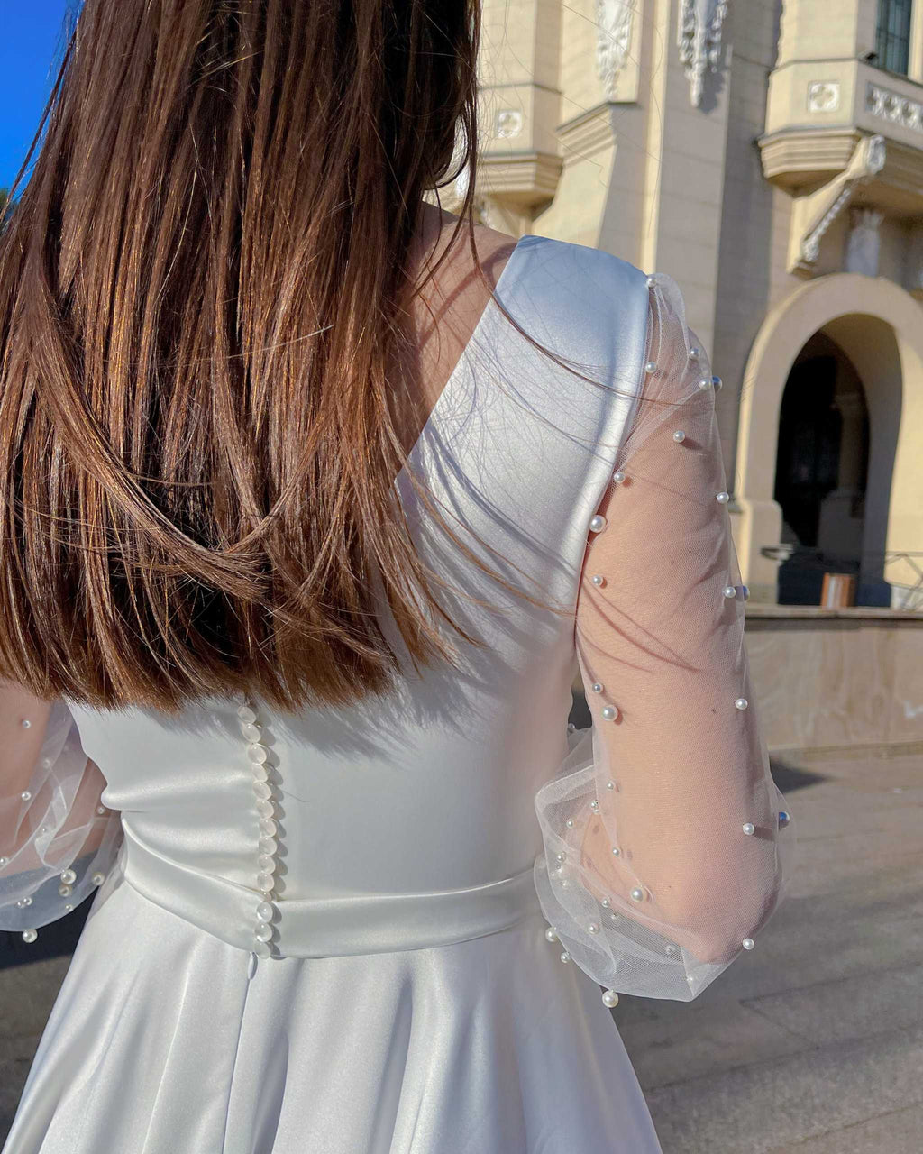 Rochie de mireasa albă lungă cu mâneci din perle, detaliu spate elegant, nasturi și tulle decorat.