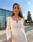 Rochie albă elegantă cu mâneci lungi și slit pe piciorul stâng, perfectă pentru evenimente speciale.