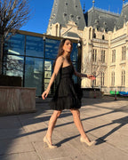 rochie cocktail elegantă scurtă neagră cu corset și șiret reglabil, fustă evazată, model purtând mărimea XS, exterior clădire istorică