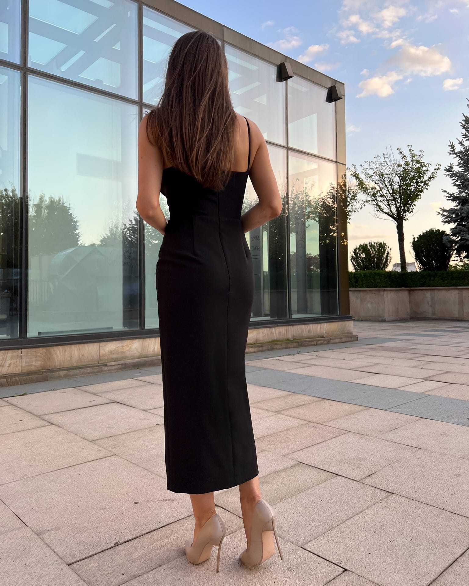 Rochie eleganta neagră de seară cu tăietură pe mijloc, croială ajustată, fermoar la spate, căptușeală interioară, model purtând mărimea XS.