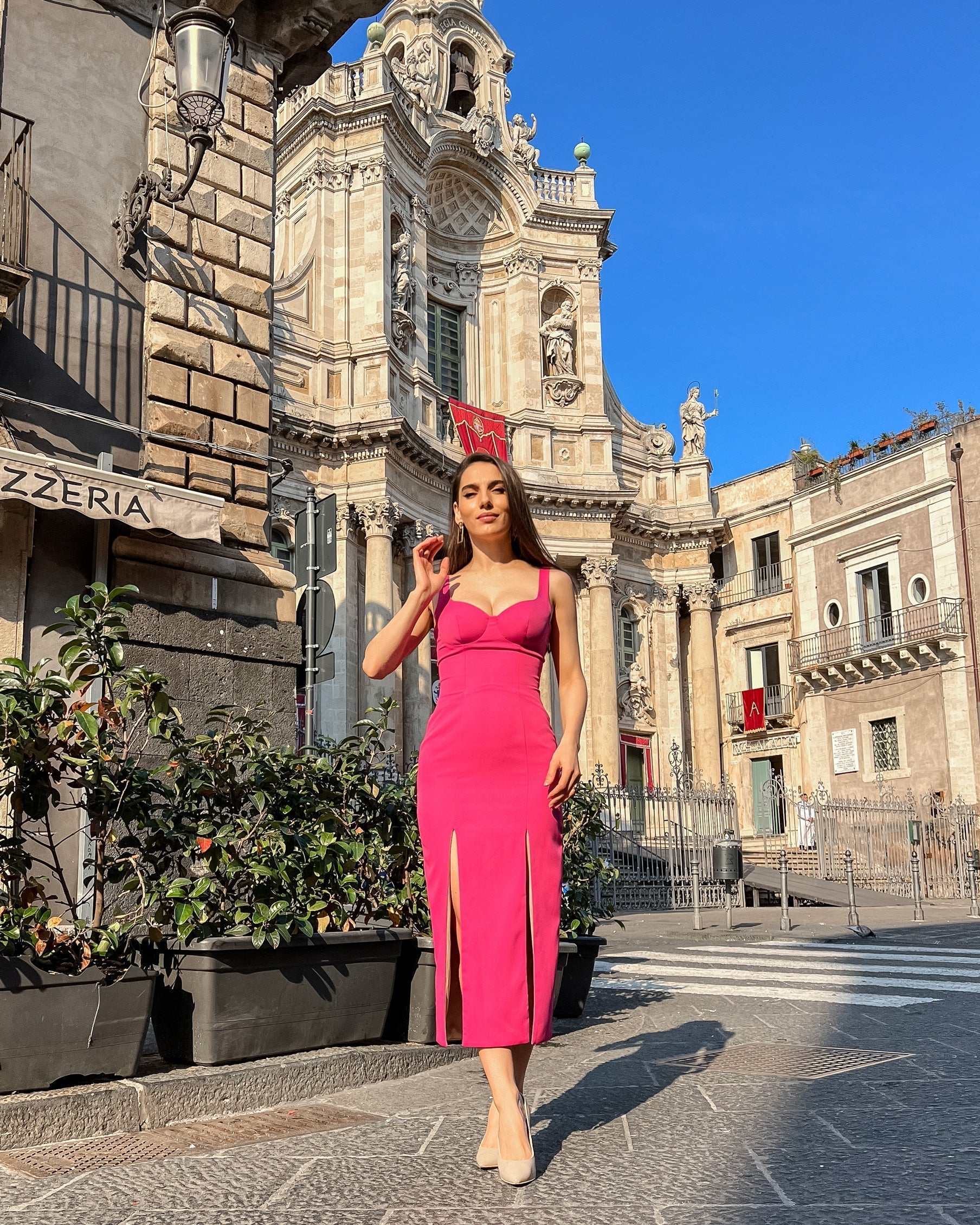 Rochie eleganta roz cu decolteu și două slituri, purtată pe stradă în fața unei clădiri impunătoare.